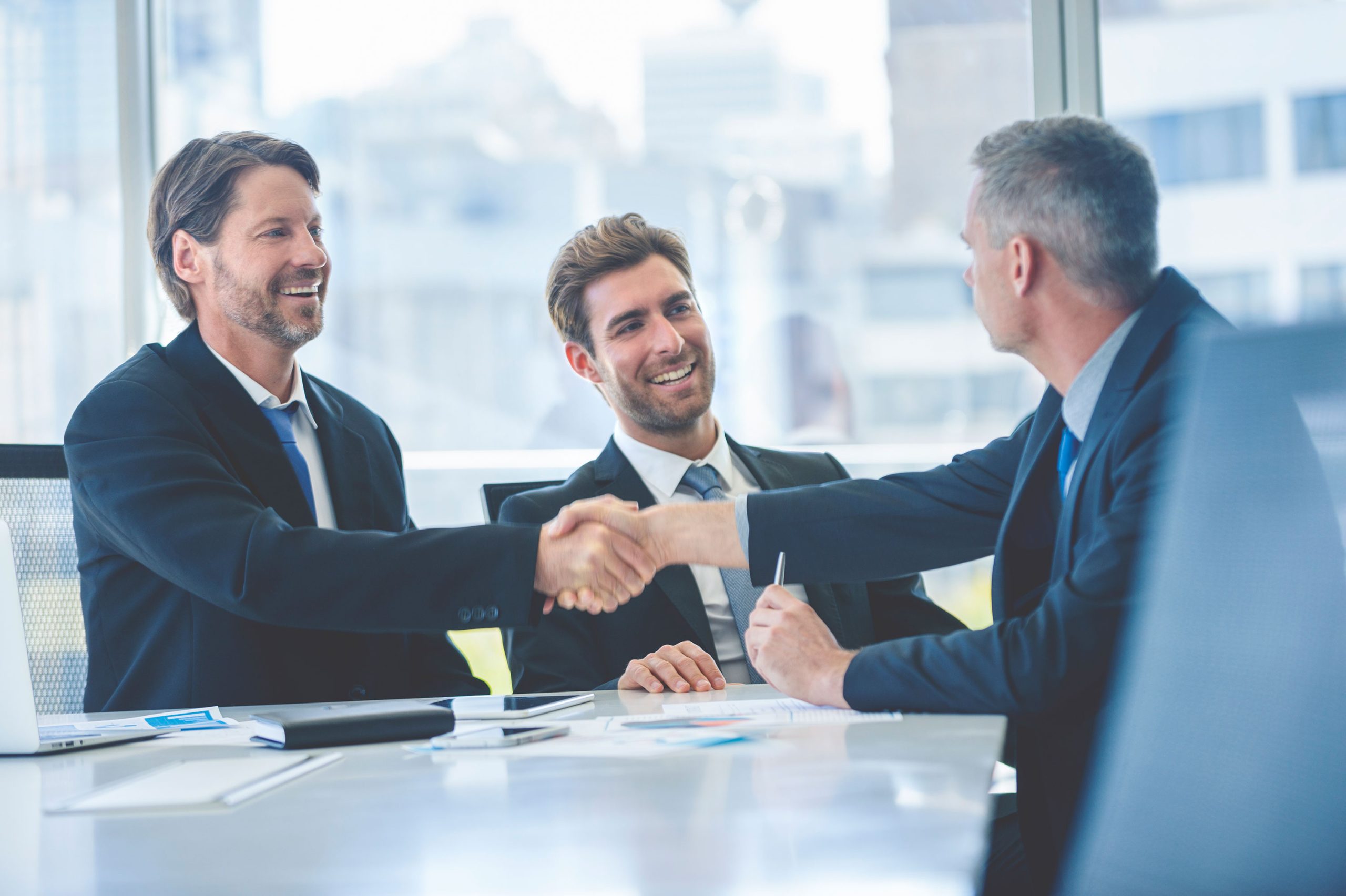 Three men in a meeting with two shaking hands